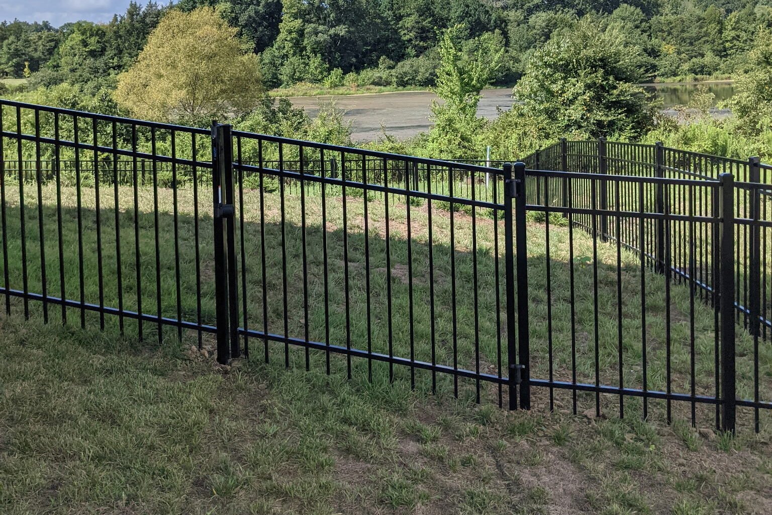 A 4' tall, 3 rail, black residential aluminum fence with a single sloped gate on a hill