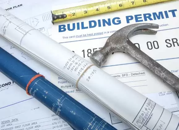 an overhead shot of a set of blueprints and building permits with a hammer on top