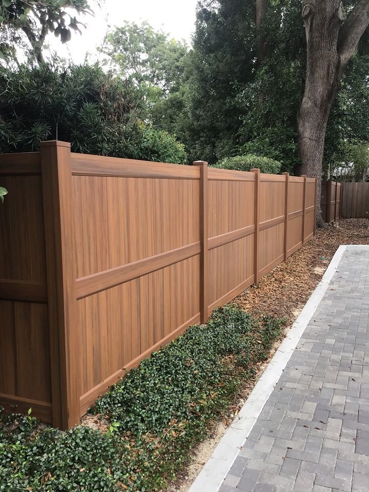 wood grain vinyl privacy fence extending past the length of a brick pathway