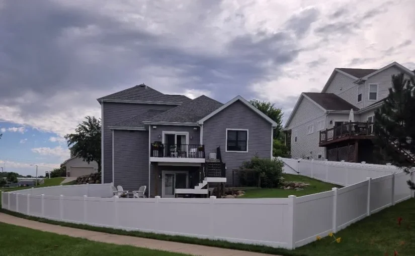 A gray two story house with a white vinyl privacy fence surrounding the back yard