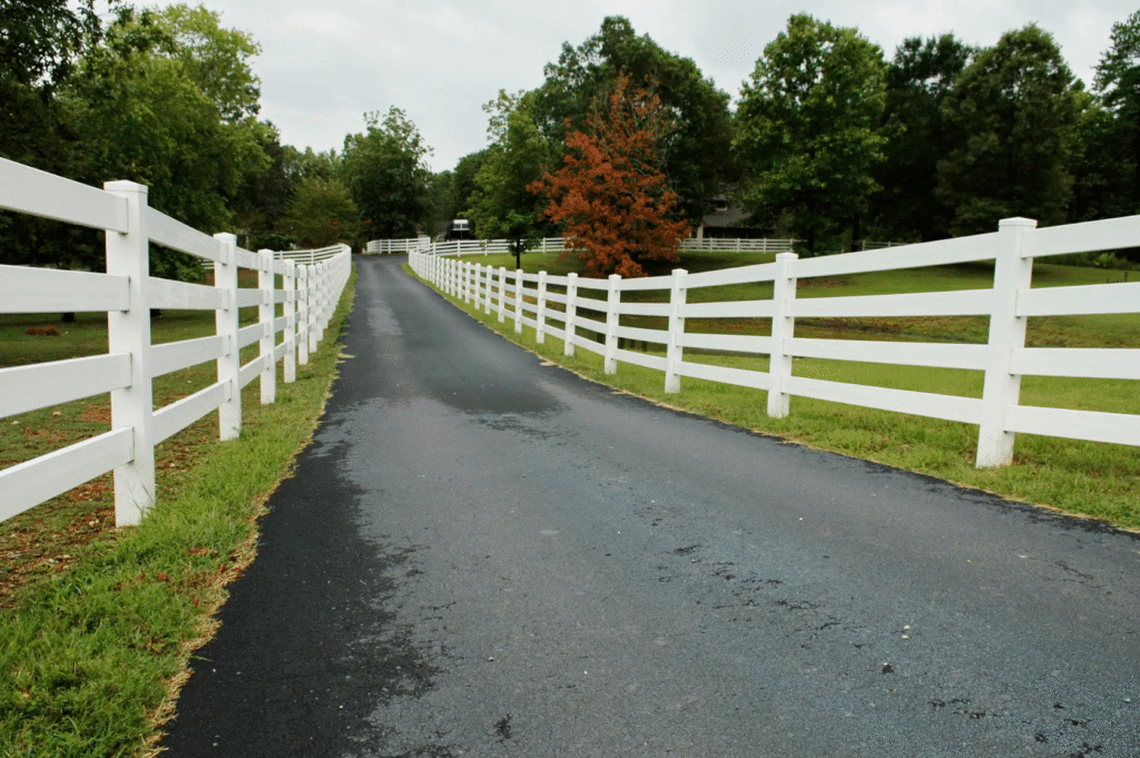 White vinyl fences in concord in a 4 rail farm fence style, extending down a paved driveway