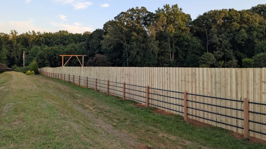 8' tall custom wood board on board fence, next to a modern metal post and rail fence