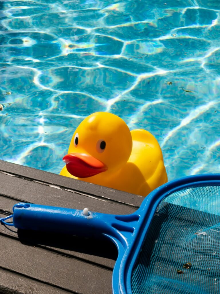 A big yellow rubber duck in a swimming pool with a pool net beside it