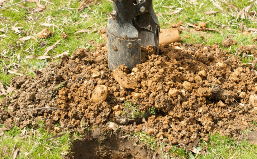 a hole being dug by a set of post hole diggers, in a residential yard prior to installing a residential fence