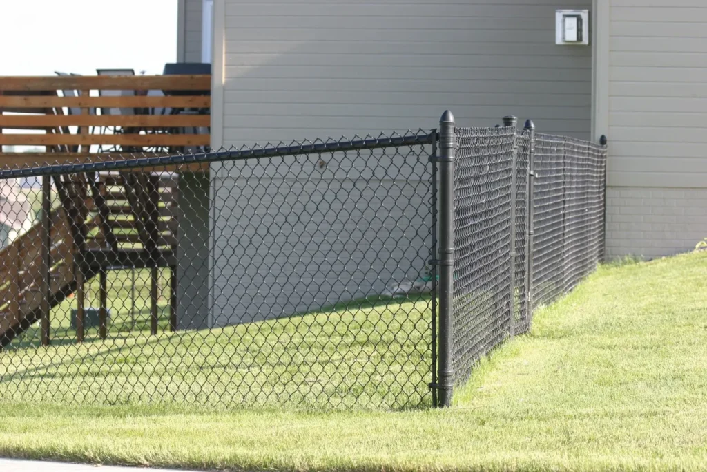 a black chain link fence installed at the back corners of house with vinyl siding and a wooden deck out back.