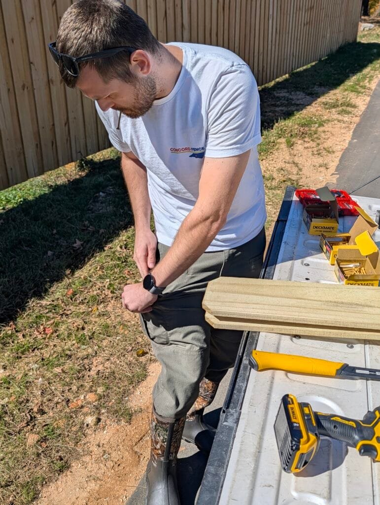Jake from Concord fence preparing to repair a board on board privacy fence. Pictured is him standing at his tailgate, putting screws in his pocket and organizing his tools on the bed of his truck.