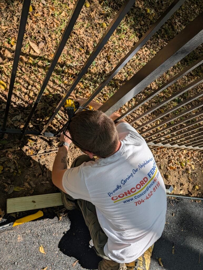 Jake from Concord Fence repairs an aluminum fence along a walking path