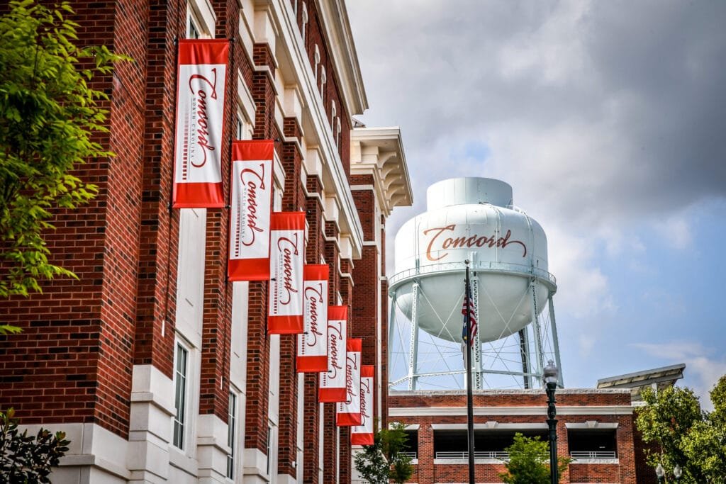 a promotional shot for Concord, NC featuring the iconic water tower and city flags lining a brick building