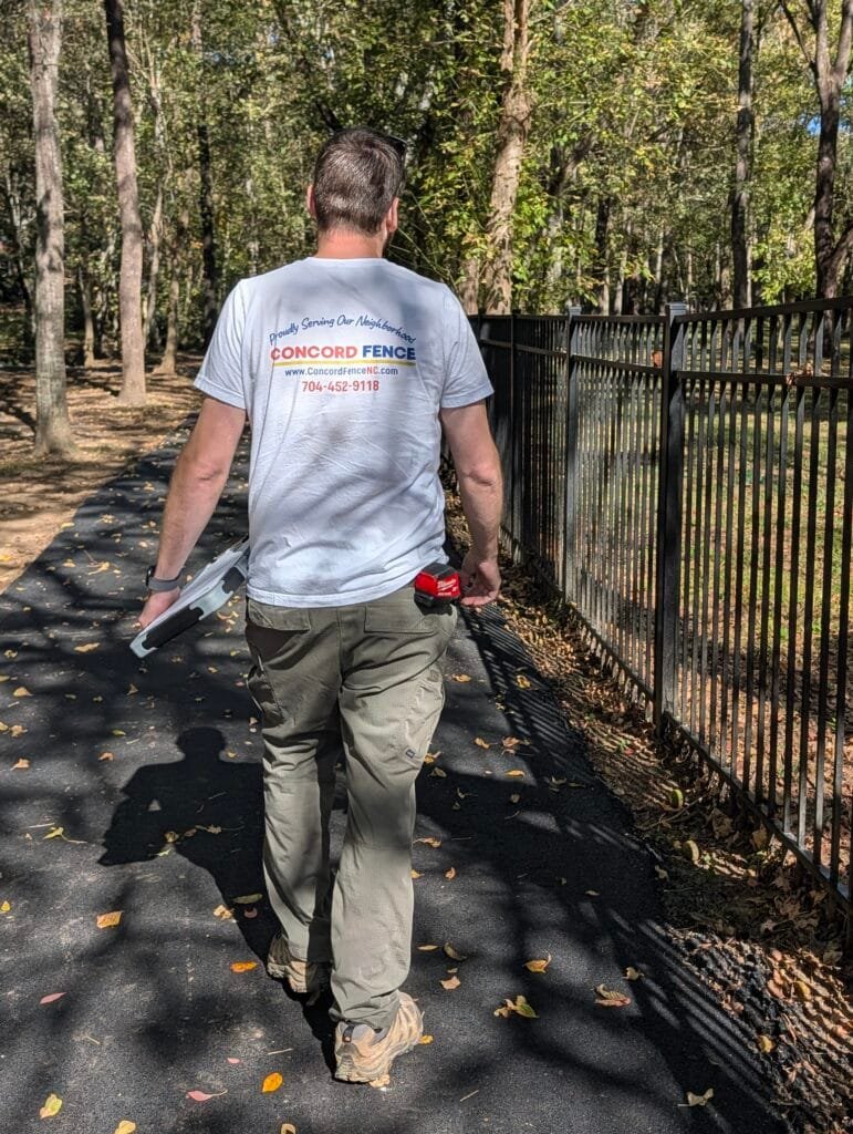 Jake from concord fence walks a greenway to assess damages on an aluminum fence lining the walkway