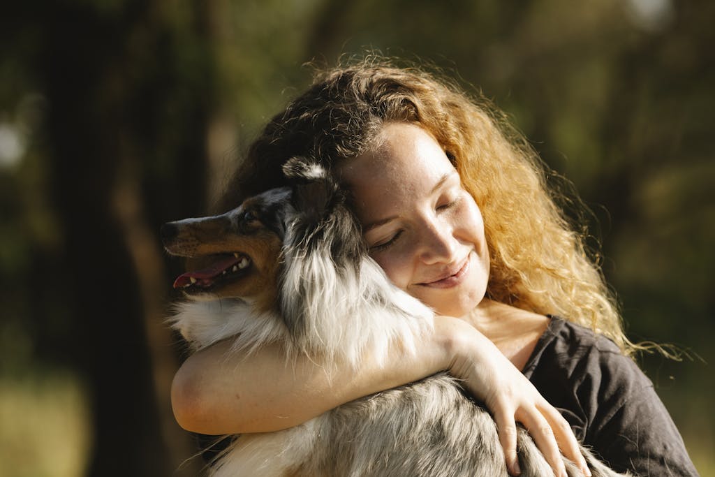 Happy woman hugging a Shetland Sheepdog in a sunny outdoor setting.