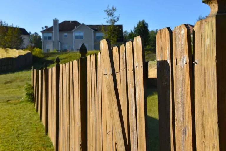 a wooden fence that is need in of repair with a residence in the background