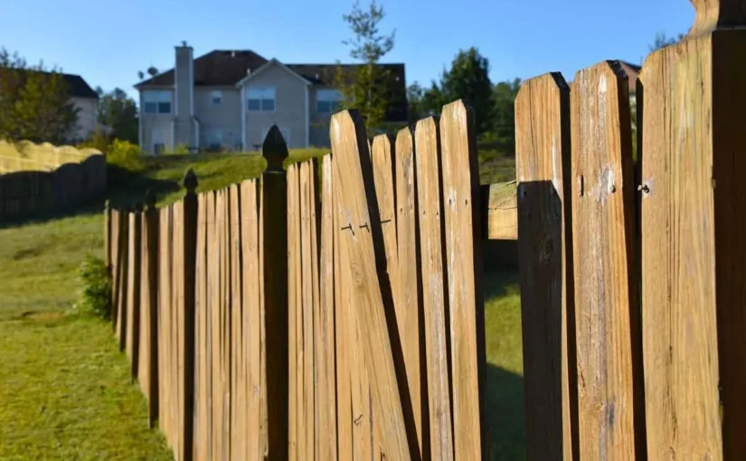 a wooden fence that is need in of repair with a residence in the background